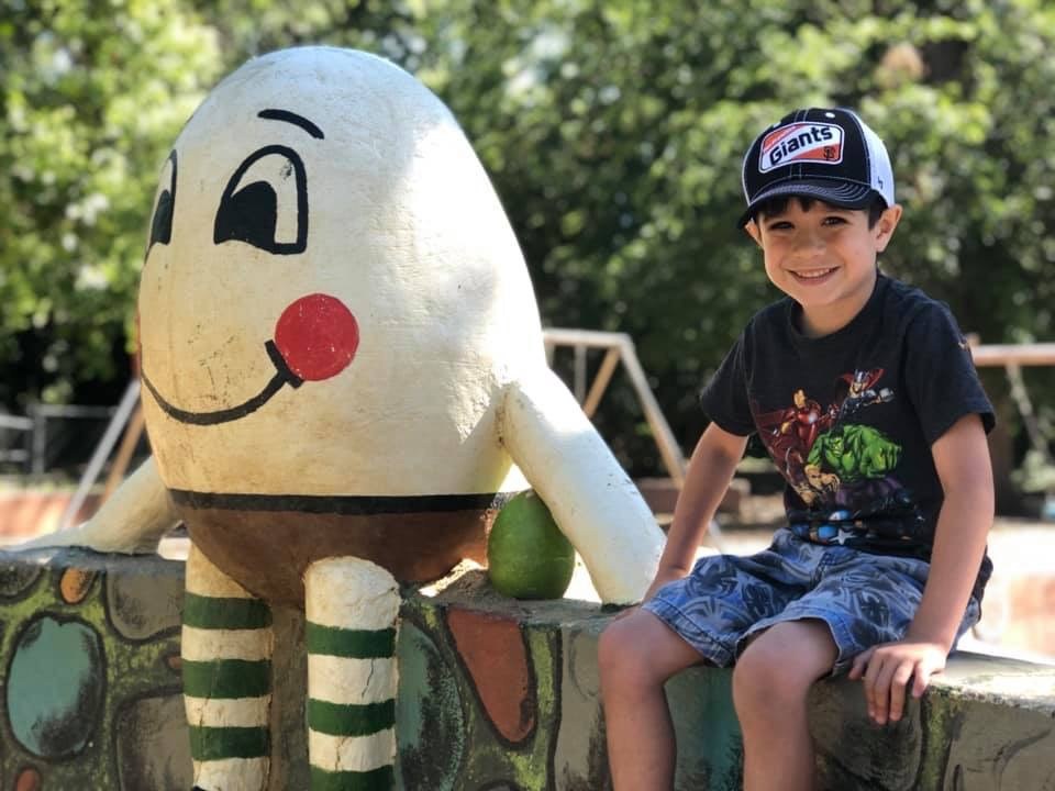 Young child seated beside the Humpty Dumpty figure at Caper Acres