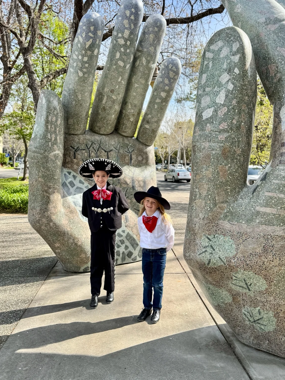 Children in traditional performance attire standing beside public art sculptures