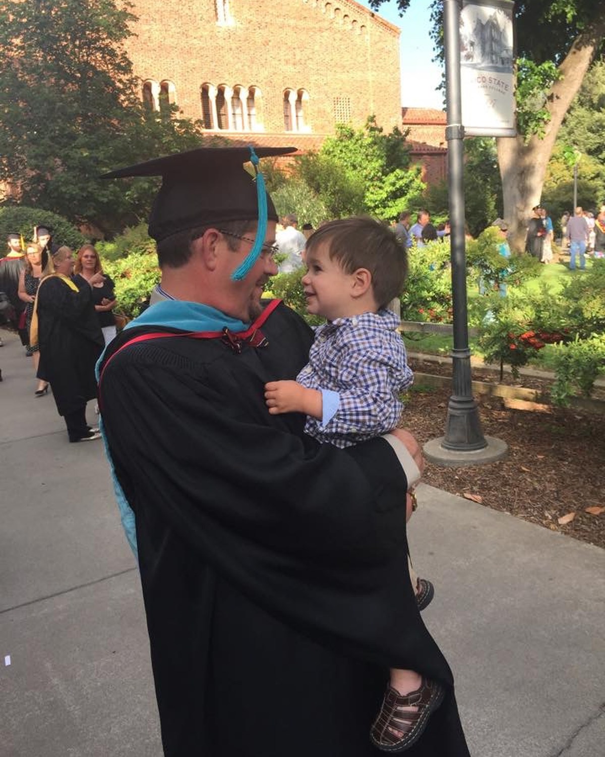 Randall Stone in academic regalia holding Rhys after his 2015 Master of Public Administration graduation and hooding ceremony
