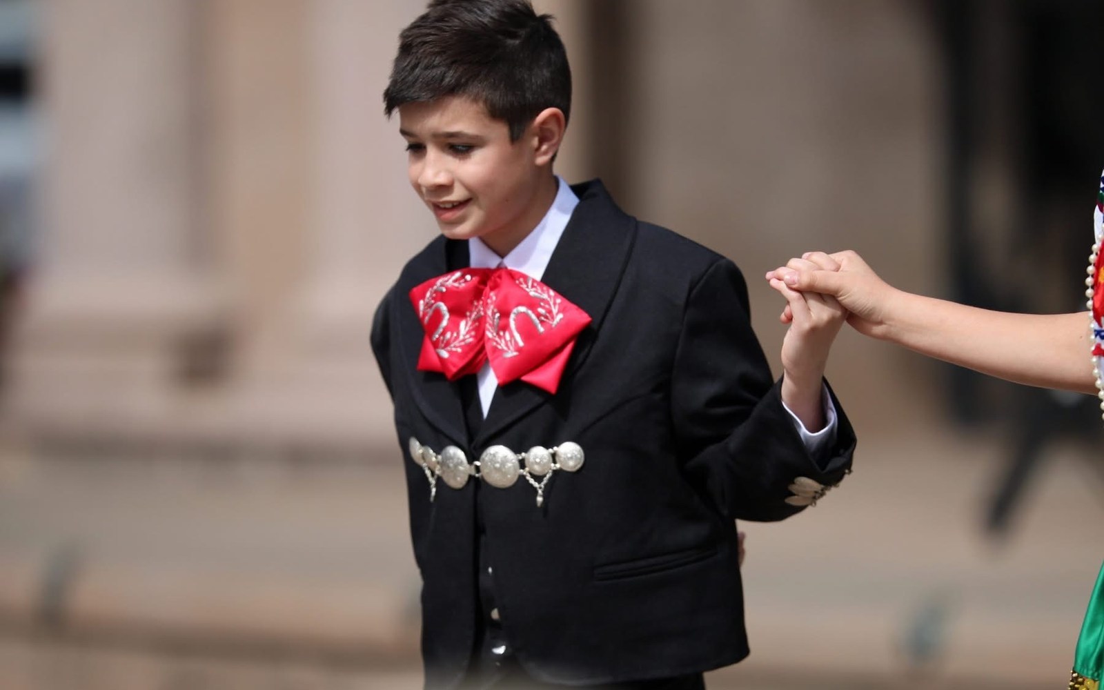 Young charro performer holding a dancer's hand during a folklórico performance
