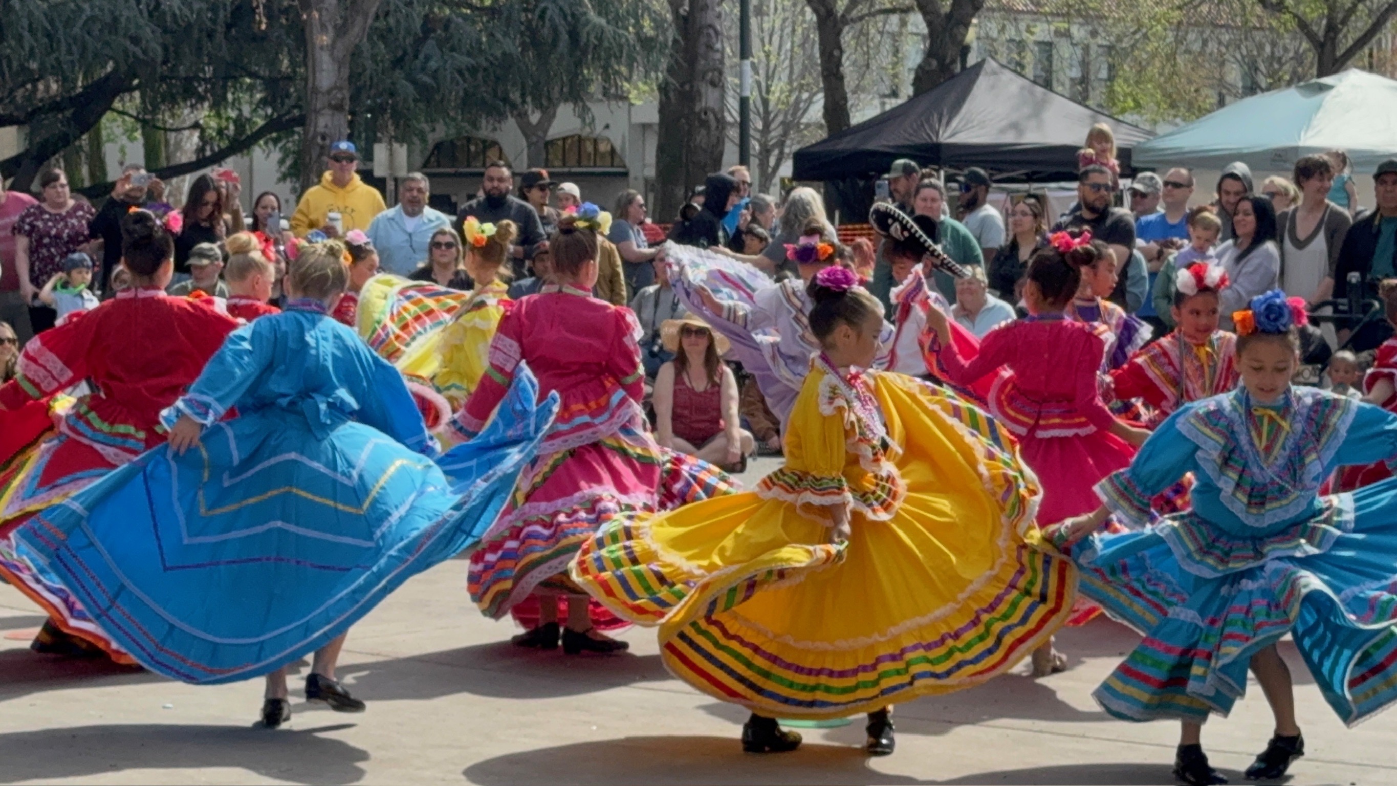 Rosas de María dancers performing in brightly colored folklórico skirts before an outdoor audience